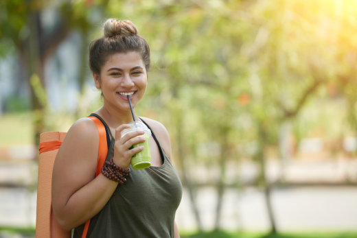 Woman smiling with yoga mat drinking green smoothie.